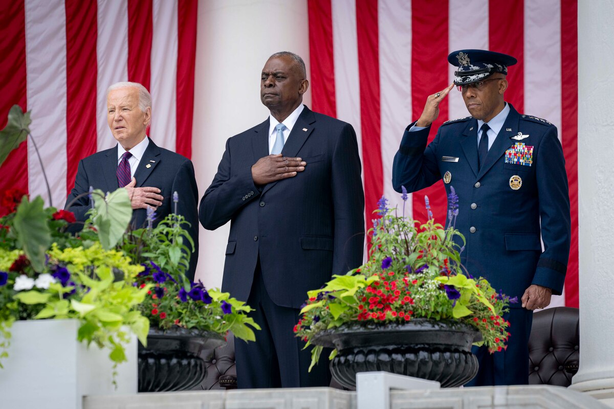 Two civilians and a military officer salute from a stage.