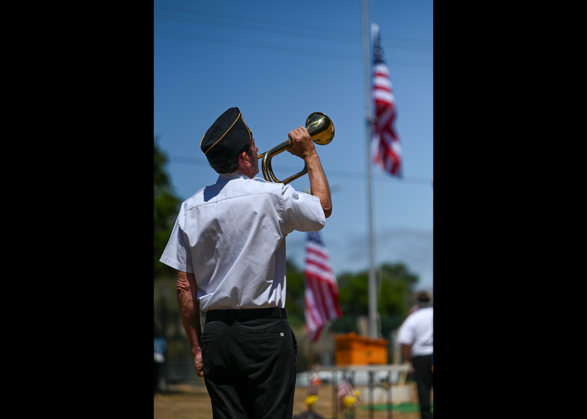 A person plays the bugle in front of the american flag.