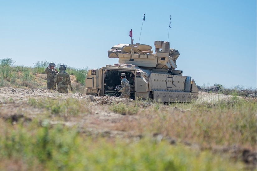 U.S. and Canadian troops train near a tank in a field.