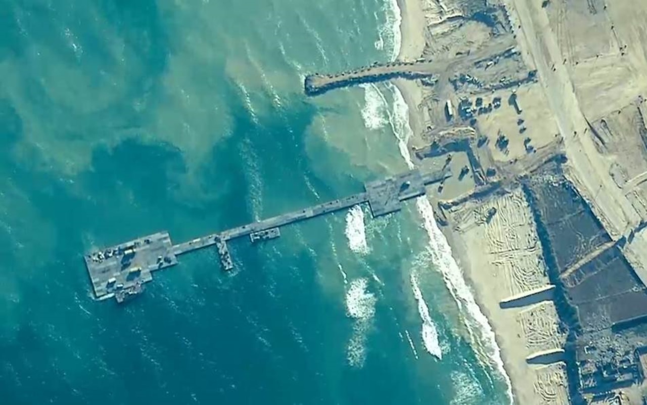 A view from space shows a long, slender, metal pier that extends from a sandy beach to roughly 800 feet out into the ocean.