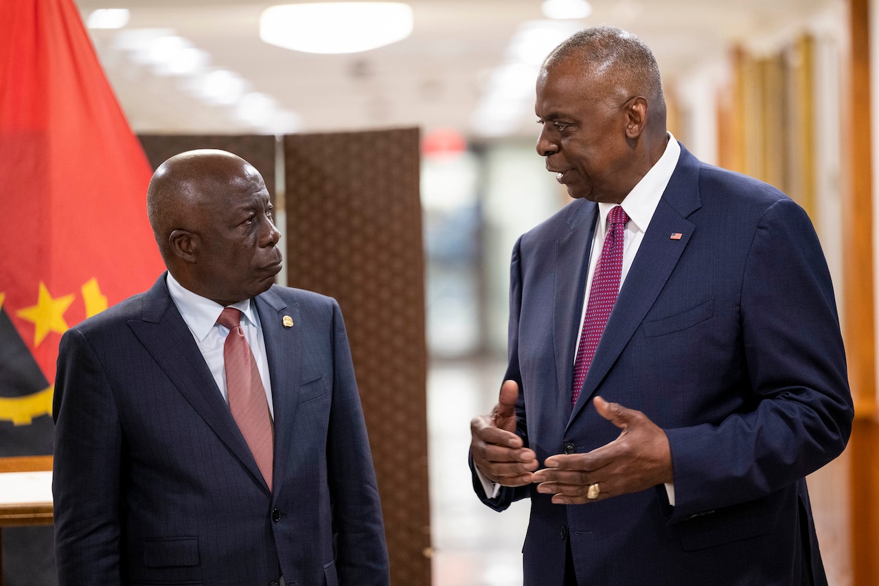 Secretary of Defense Lloyd J. Austin III speaks with another civilian while standing in a hallway.