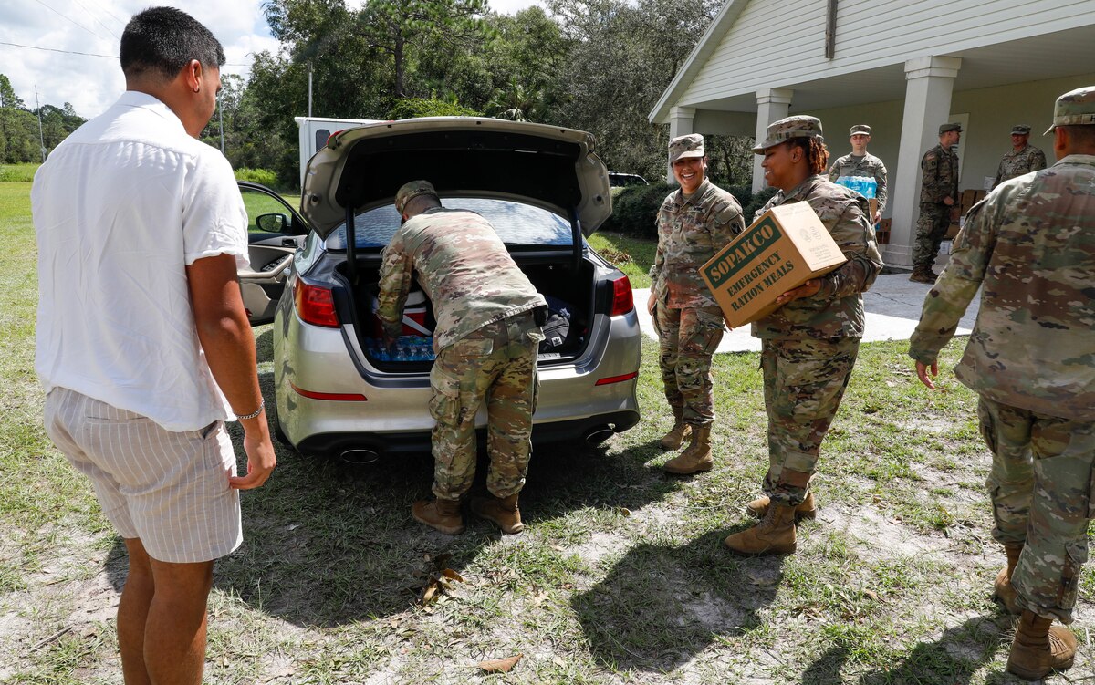 Soldiers load boxes into the trunk of a car.