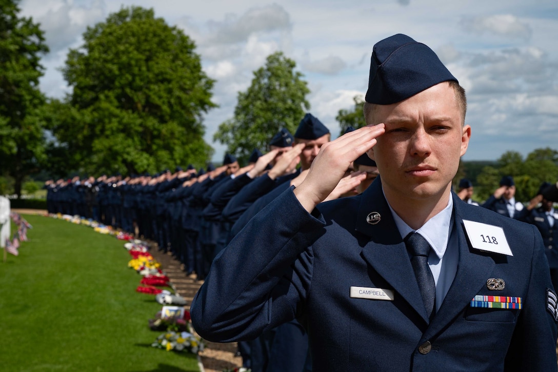 Lines of service members salute while standing on a pathway edged with flowers.