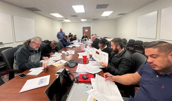 A man standing over a table with a dozen people seated. The man standing, Mitch Jackson, is providing them with training.