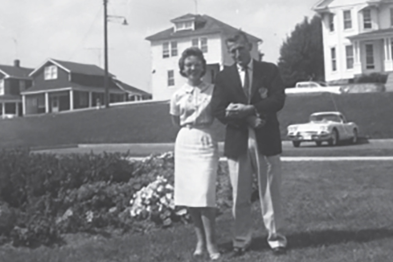 A person holds another's arm while posing for a photo. The two stand on a lawn.