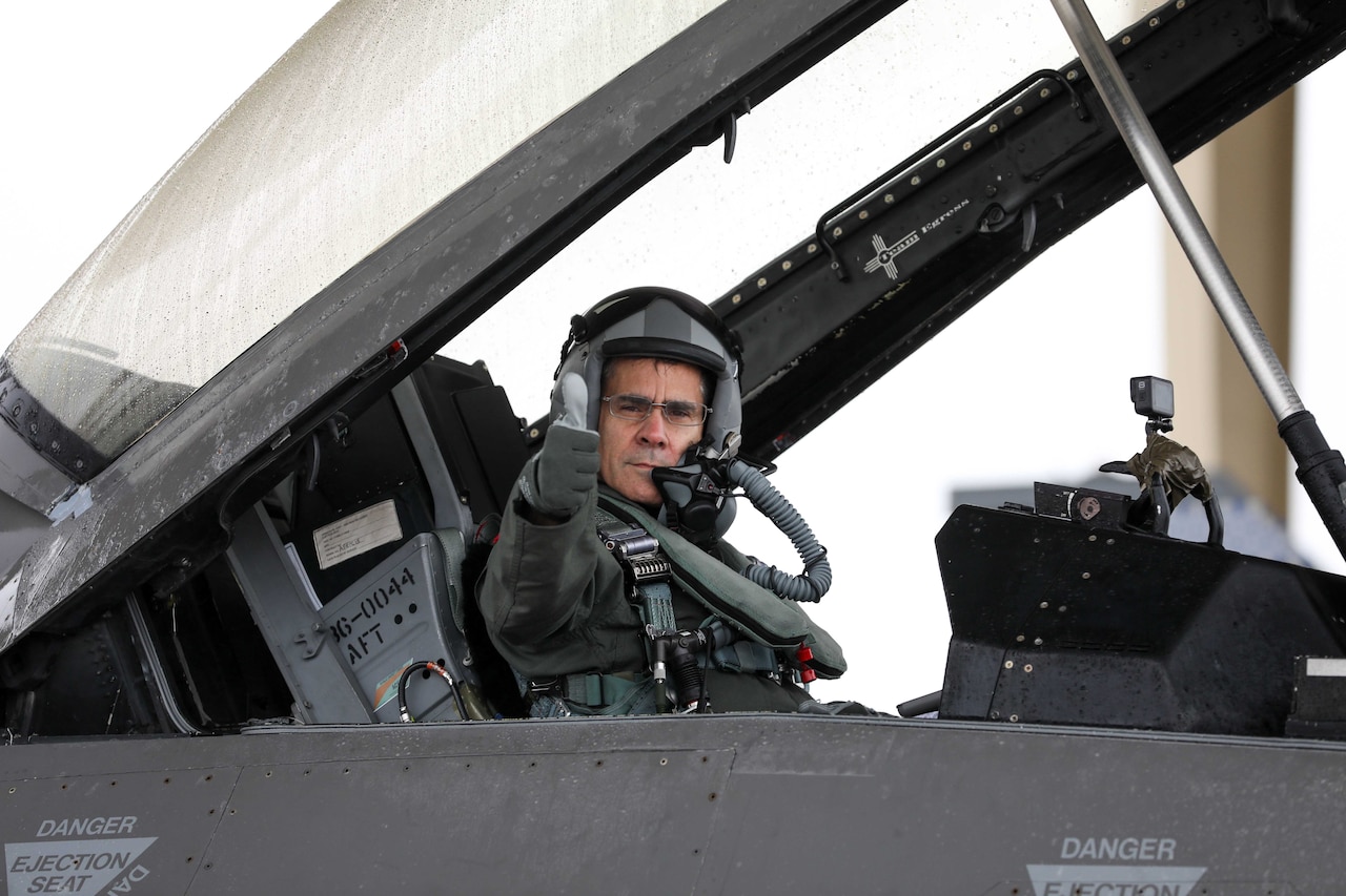 A pilot gestures from a jet cockpit.