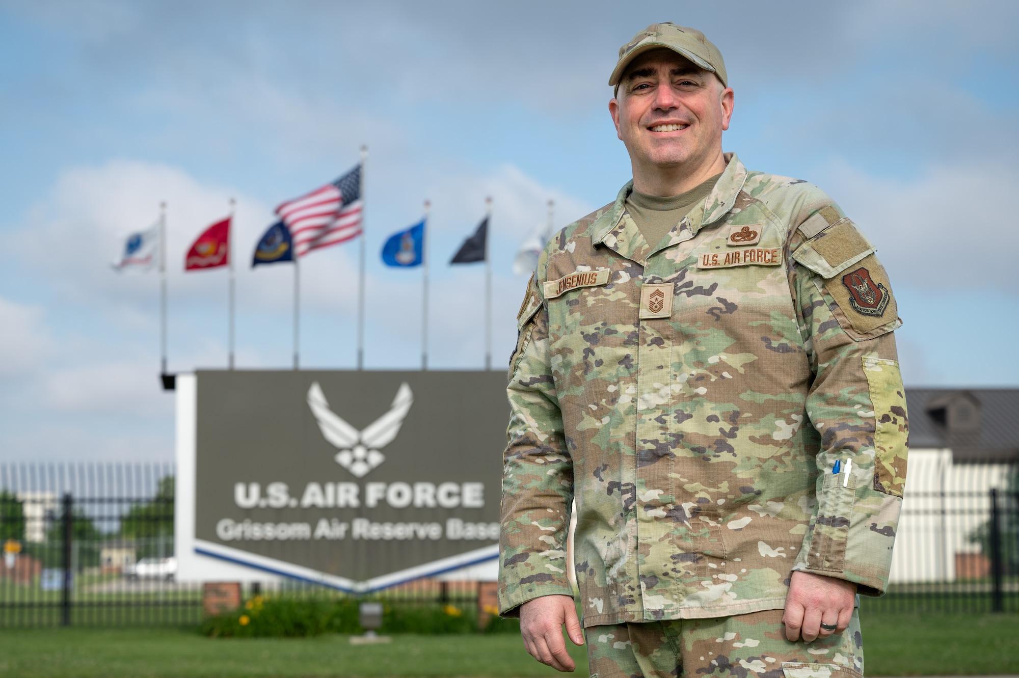 A man in a U.S. Air Force duty uniform stands in front of a sign in the distance that reads "U.S. AIR FORCE" "Grissom Air Reserve Base".