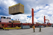 Sailors move a large container off of a ship onto the pier.