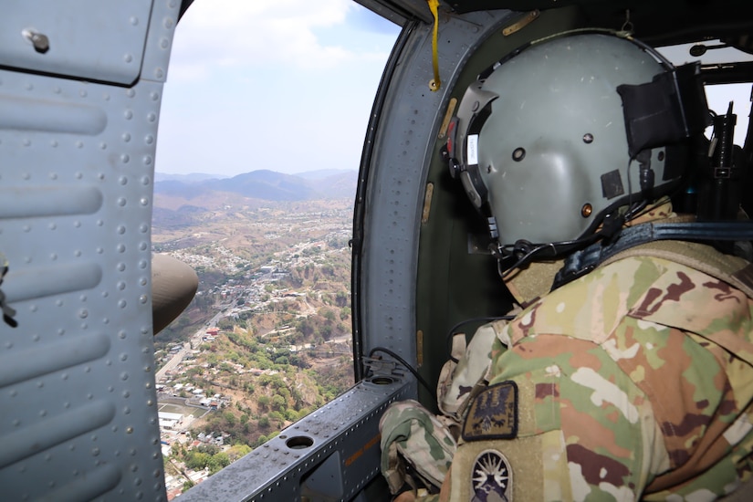 A soldier looking out a window of a helicopter.