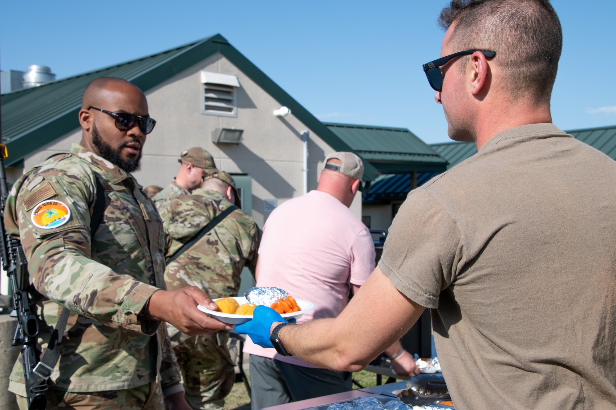 U.S. Air National Guard Airman distributes food in serving line to an Airman wearing OCP uniform