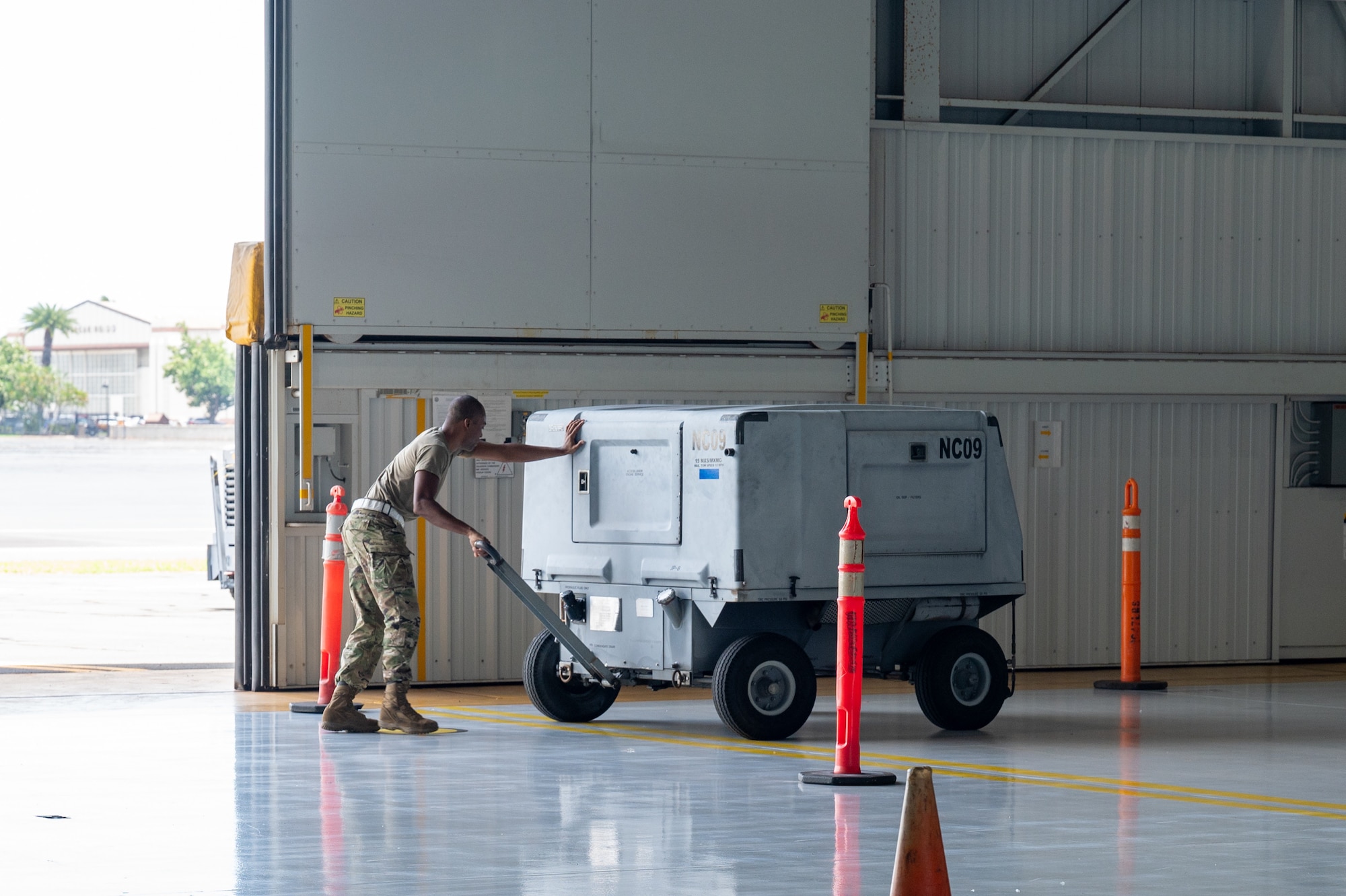 An Airman pulls a generator on wheels through an obstacle course inside a hangar during a morale event.
