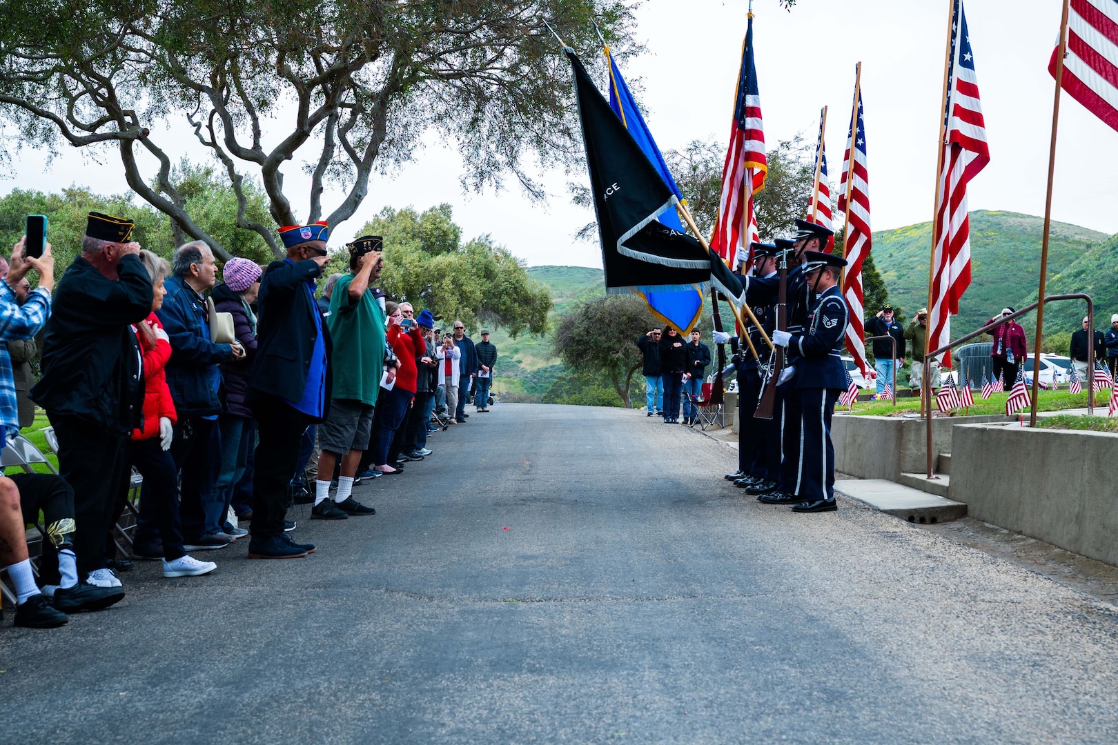 Ceremony attendees stand and look at the presentation of military flags by honor guard members during a Memorial Day ceremony.