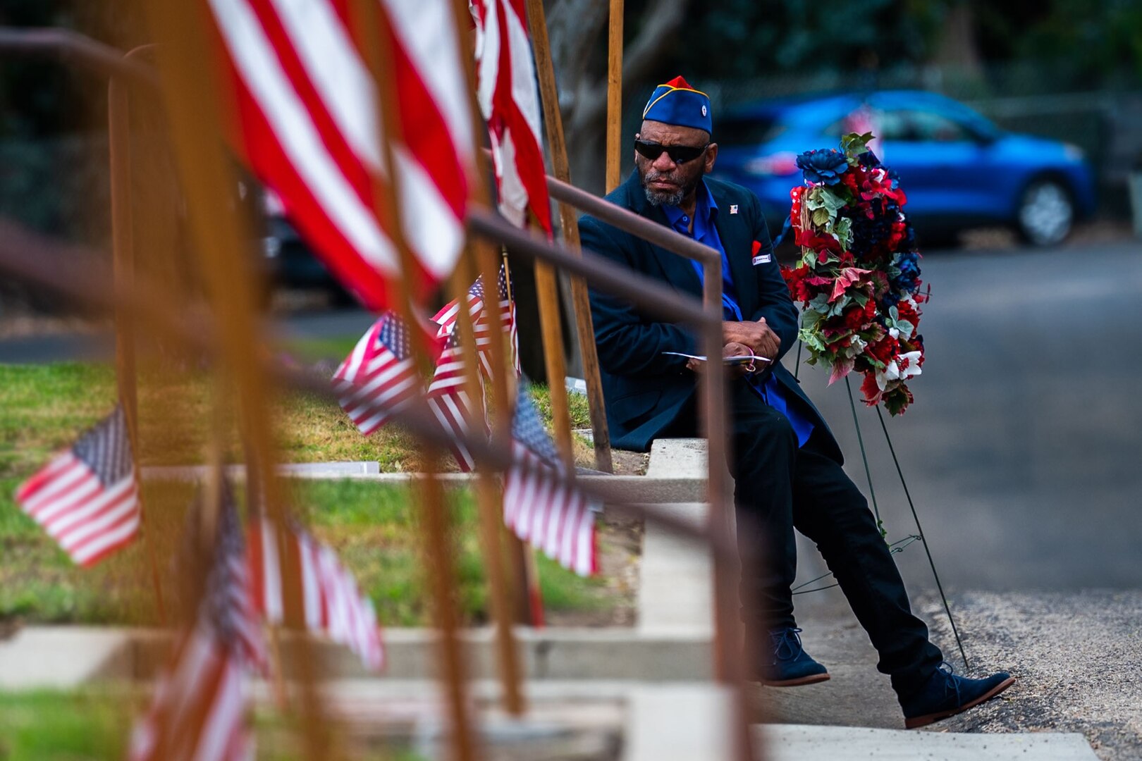 A man sits next to a wreath during a Memorial Day ceremony at a cemetery.