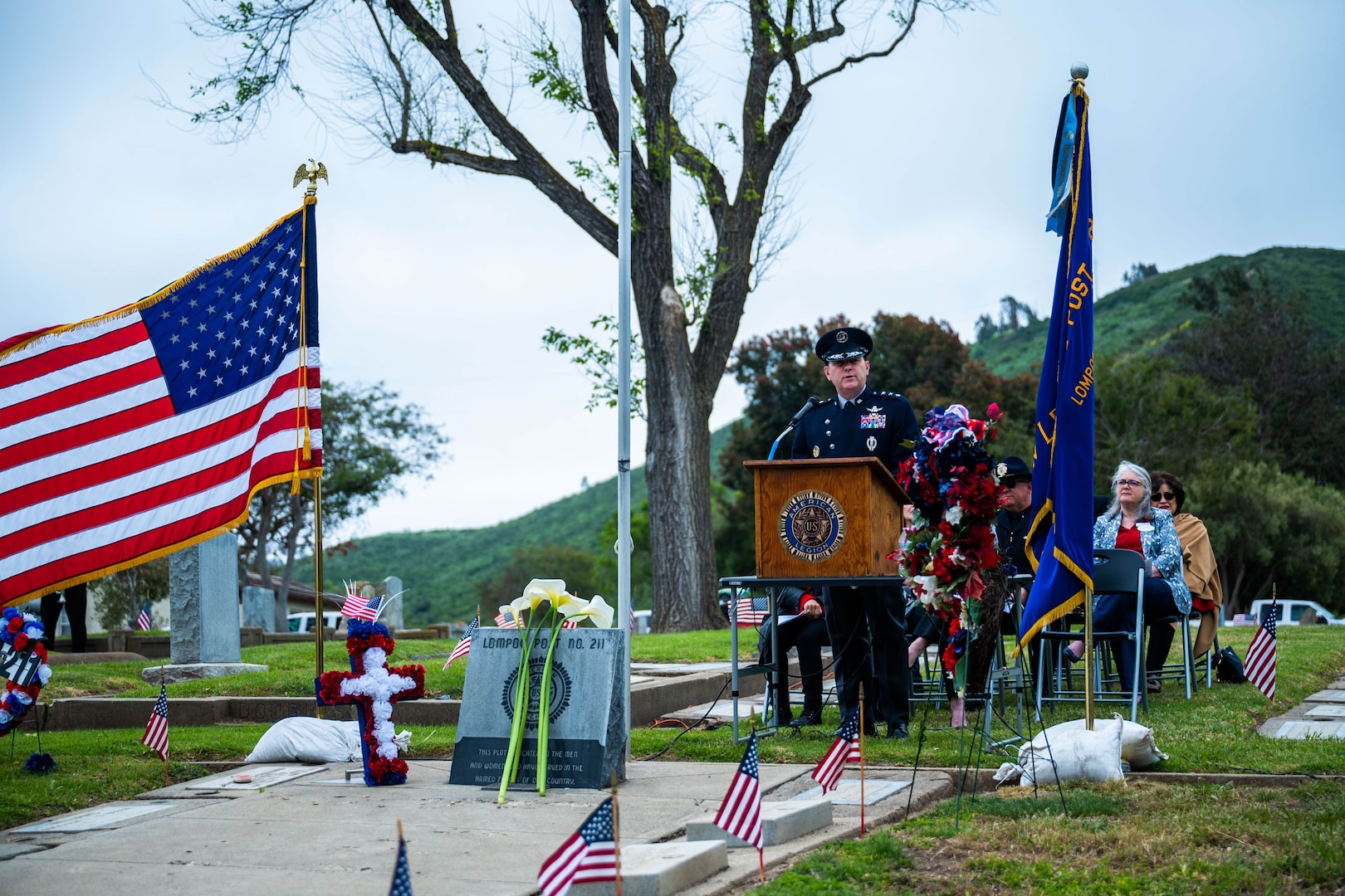 A general gives a speech at a podium in the middle of a cemetery surrounded by American flags.