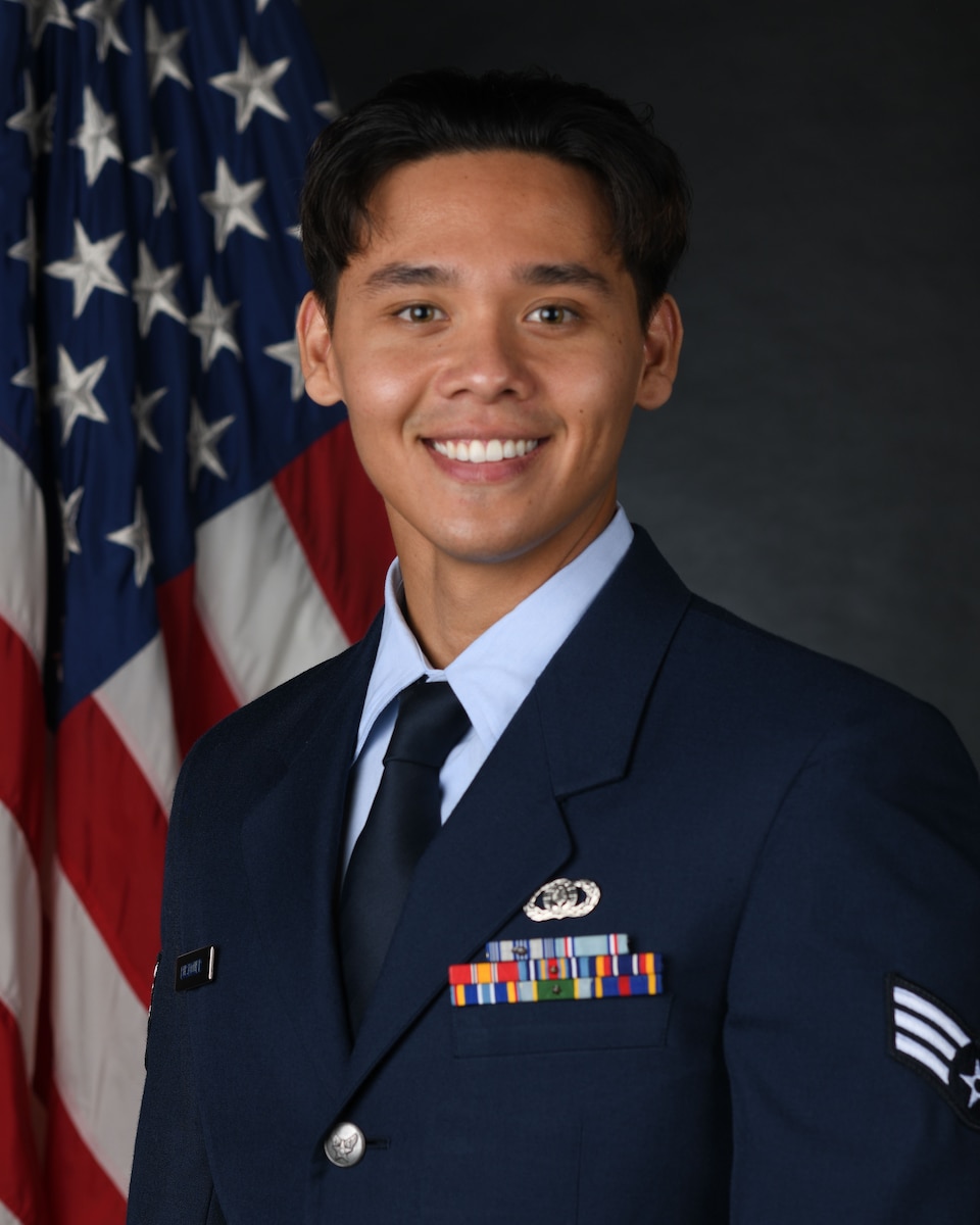 Official photo of SrA Keegan Bushouer, vocalist.  SrA Bushouer is wearing blue service dress and standing in front of the American flag.