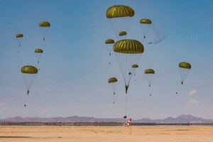 U.S. and Moroccan soldiers free-fall in tandem with parachutes into a desert-like area with mountains in the background.