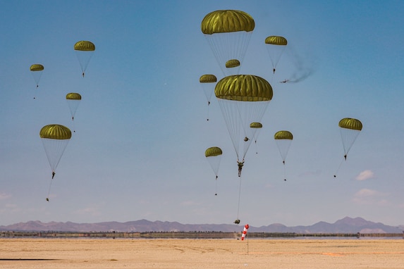 U.S. and Moroccan soldiers free-fall in tandem with parachutes into a desert-like area with mountains in the background.