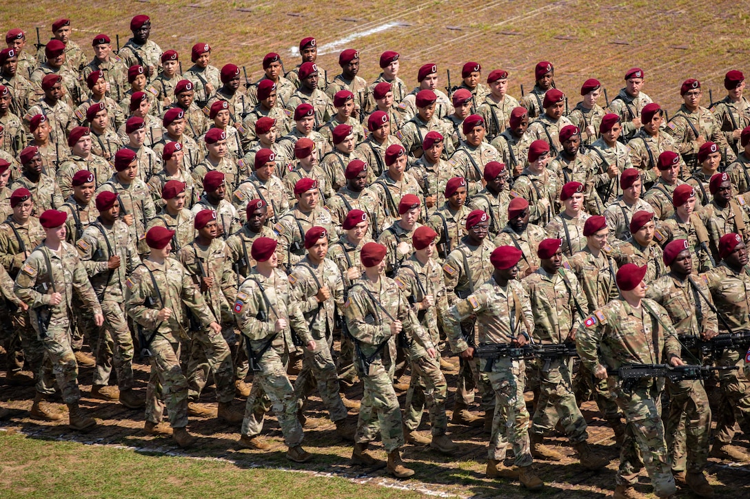 Paratroopers wearing maroon berets carry weapons as they march in formation.