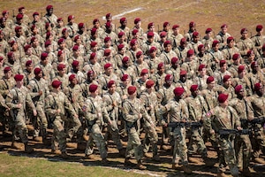 Paratroopers wearing maroon berets carry weapons as they march in formation.