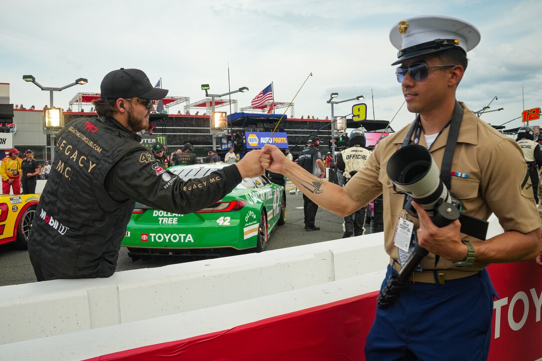 U.S. Marine Corps Lance Cpl. David Ornelas-Baeza, from Texas, and a combat videographer with Marine Wing Headquarters Squadron (MWHS) 2, is greeted by a NASCAR crewmember during the Coca-Cola 600 at Charlotte Motor Speedway in Concord, North Carolina, May 26, 2024. The U.S. Marine Corps supported the Coca-Cola 600, a NASCAR race held during Memorial Day weekend, with static displays of military aircraft, vehicles and participation in ceremonies.  (U.S. Marine Corps photo by Cpl. Emily Hazelbaker)