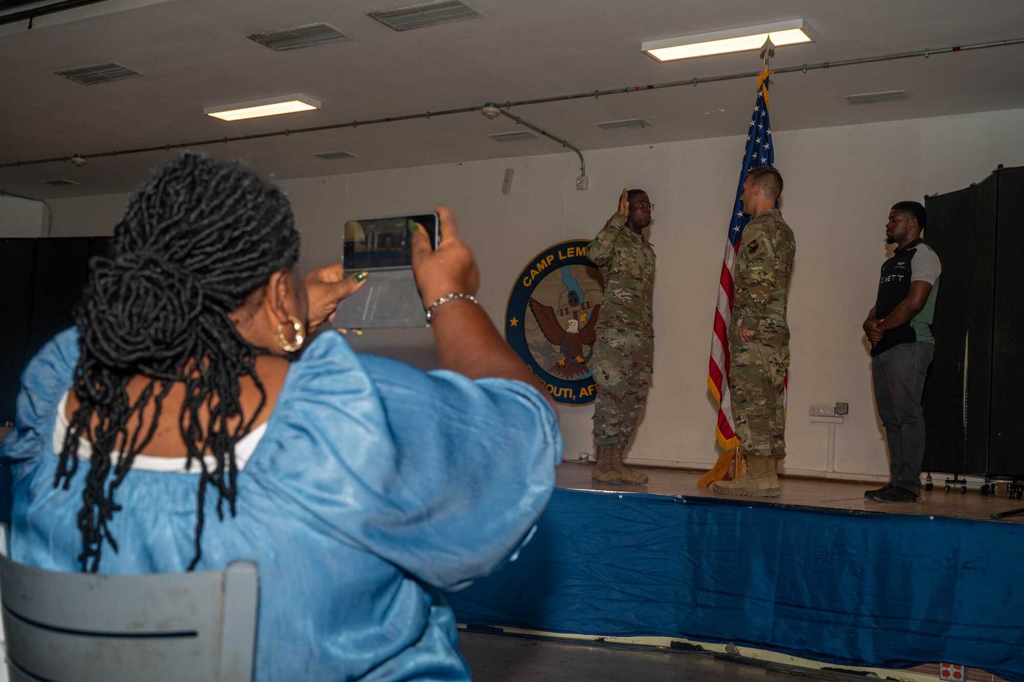 A women sitting in the crowd of a U.S. military promotion ceremony takes a photo on her phone