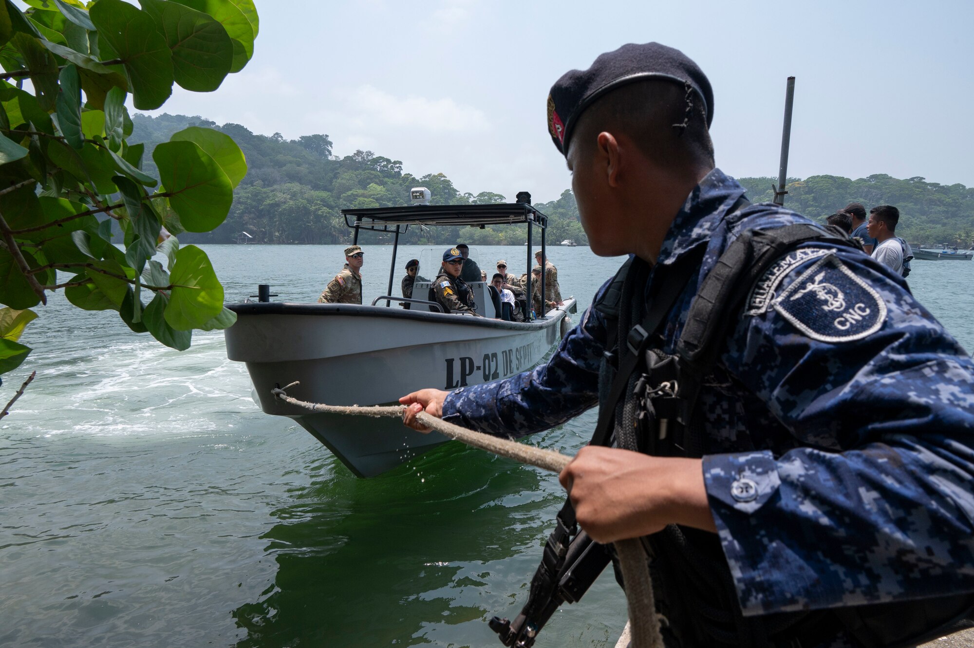 A photo of a Guatemalan marine pulling a navy fast boat with people aboard by a rope.