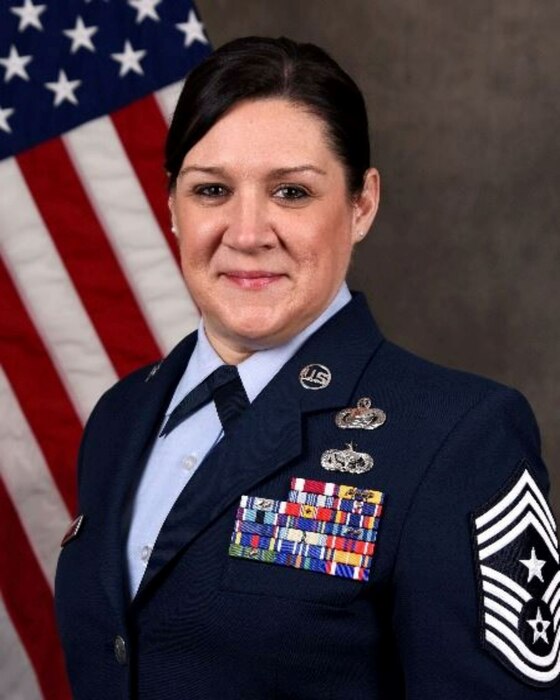 Service member smiles for official portrait in front of US flag wearing their service dress blues