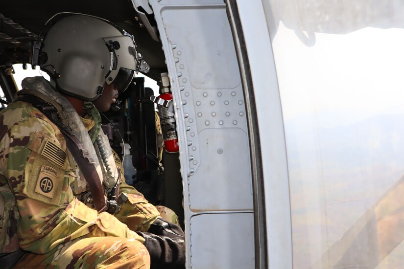 A photo of a soldier looking out a window of a helicopter.