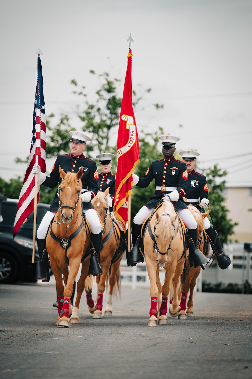 Marines in ceremonial dress ride horses while carrying flags.