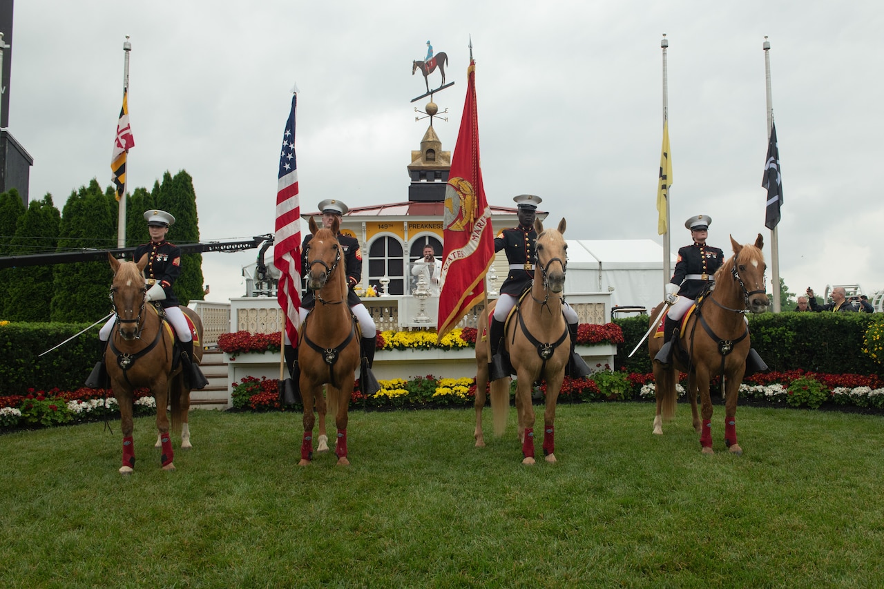 Marines in ceremonial dress sit on horses while posing for a photo in front of a building.