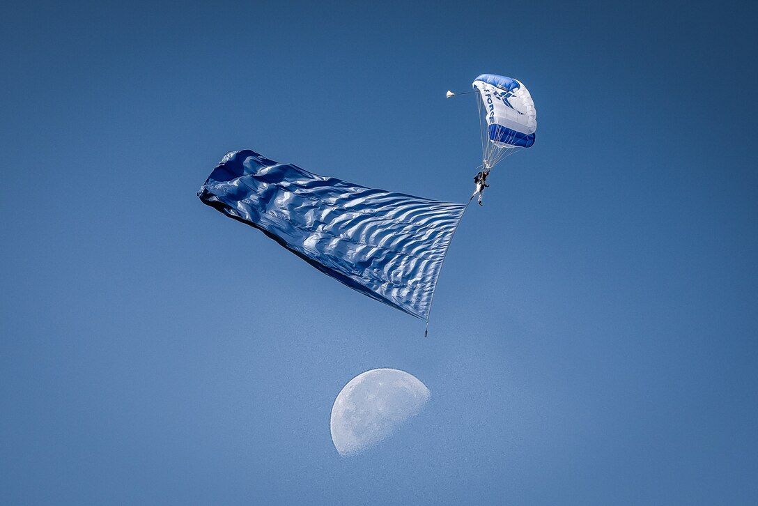 A person descends under a parachute against a blue sky.