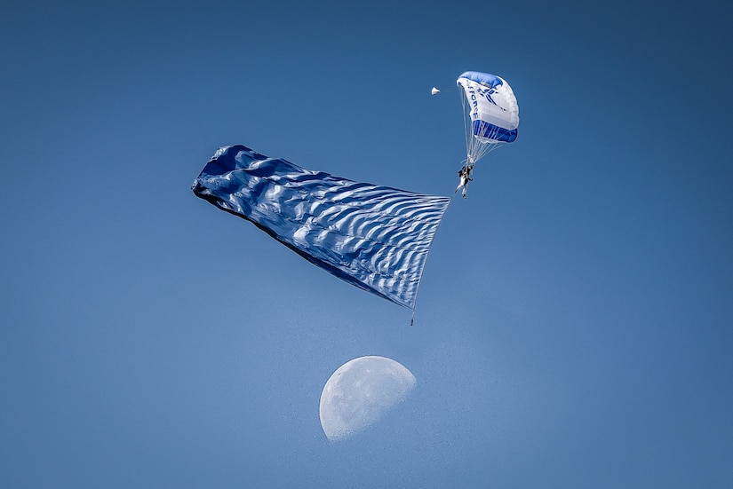 A person descends under a parachute against a blue sky.