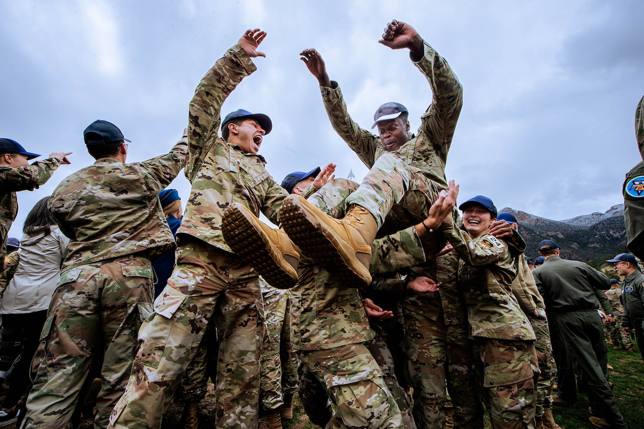 Service members in uniform hoist another service member holding his hands in the air.