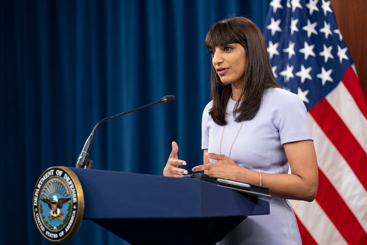 A person speaks from a podium with an American flag in the background.