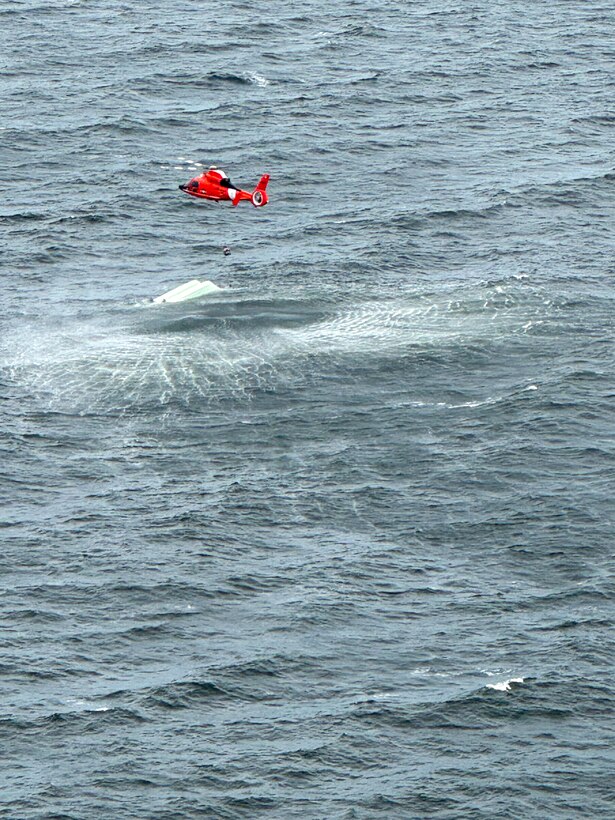 A Coast Guard MH-65 dolphin helicopter from Aviation Training Center Mobile hovers over a capsized vessel near Dauphin Island, Alabama, May 30, 2024. The Coast Guard received a sos signal from a satellite communicator one of the distressed boaters used. (U.S. Coast Guard photo by Petty Officer 3rd Class Ryan Reed)