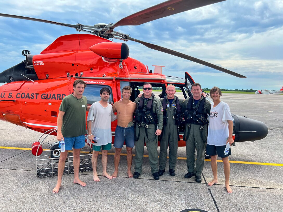 A Coast Guard MH-65 dolphin helicopter crew stands with 4 survivors at Aviation Training Center Mobile in Mobile, Alabama, May 30, 2024. The Coast Guard rescued the four boaters after their vessel reportedly capsized that day.