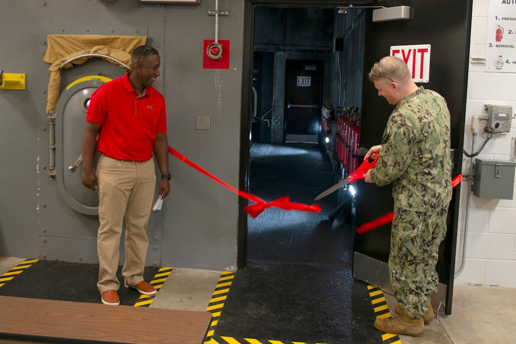 Capt. Brian Turney, commanding officer, Trident Training Facility Kings Bay, cuts a ribbon during the reopening a next generation fire-fighting trainer aboard Naval Submarine Base Kings Bay, Georgia.