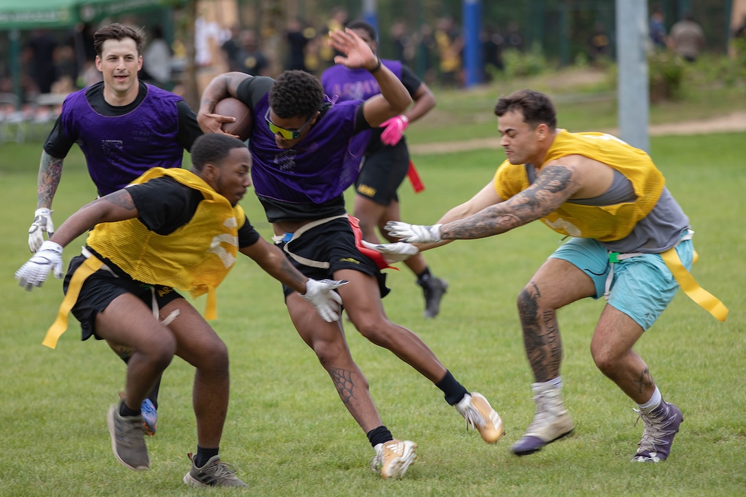 A soldier evades two defenders during a flag football game.