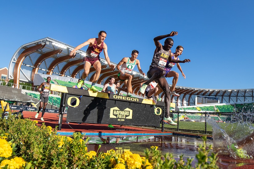 Runners jump over water during an outdoor track and field competition.