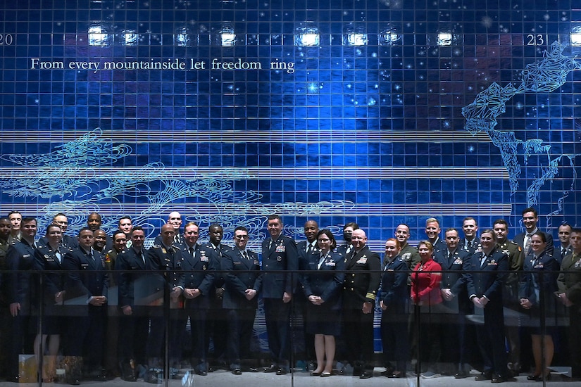 A group of service members pose for a photo in front of a blue wall that reads "From every mountainside let freedom ring."
