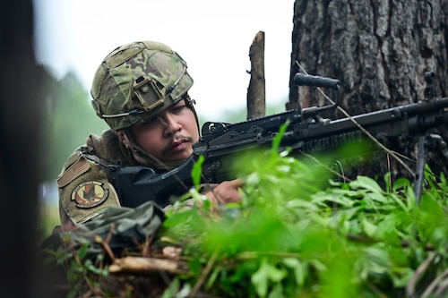 Airmen aiming with a rifle in the woods.