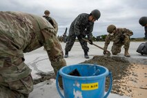 Airman and Japan Air Self Defense Force Airman smooth out concrete