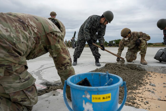 Airman and Japan Air Self Defense Force Airman smooth out concrete