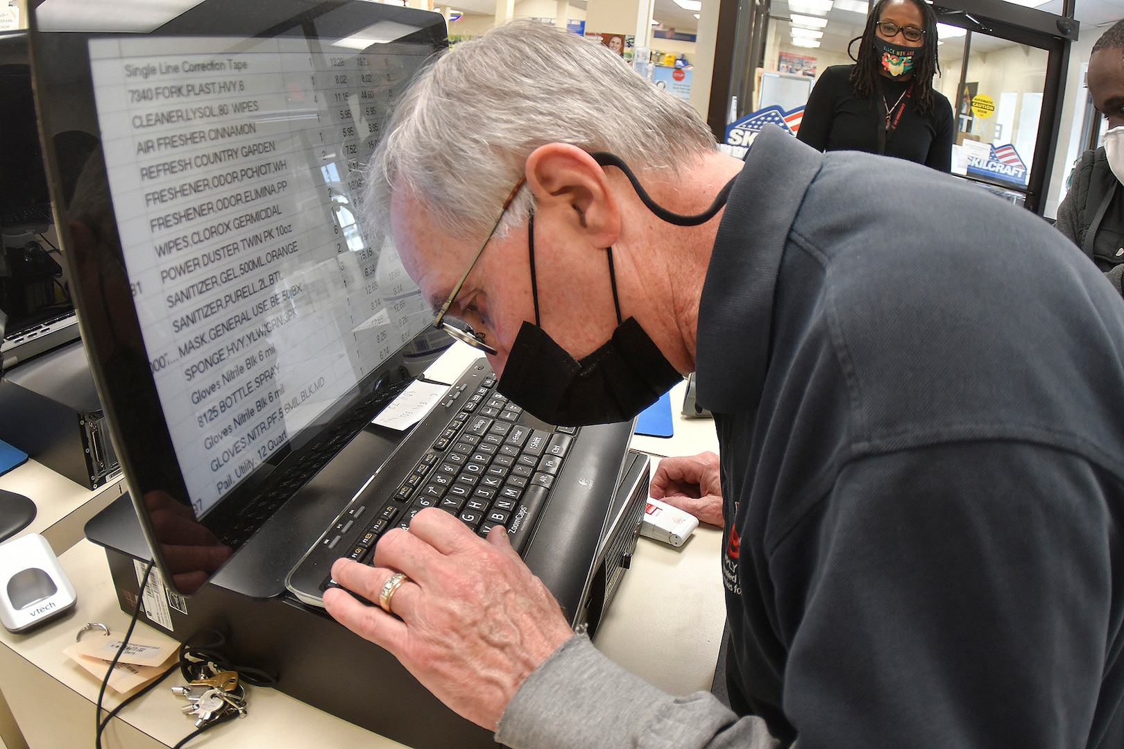 Senior wearing face mask leans over and types on keyboard.