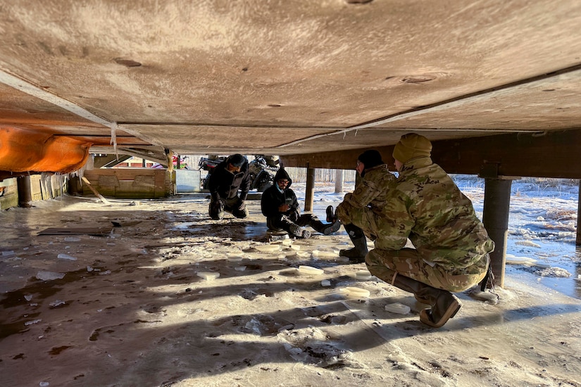 Alaska Organized Militia and volunteers crawl beneath a flood-damaged home and inspect the damage.