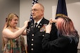 U.S. Army Col. Kevin Jones stands at attention as his daughters, Samantha and Sandra, attach his new rank to his uniform at Boone National Guard Center in Frankfort, Kentucky, Oct. 7, 2024. Jones was promoted from lieutenant colonel to colonel in front of his family and friends. (U.S. Army National Guard photo by Andy Dickson)