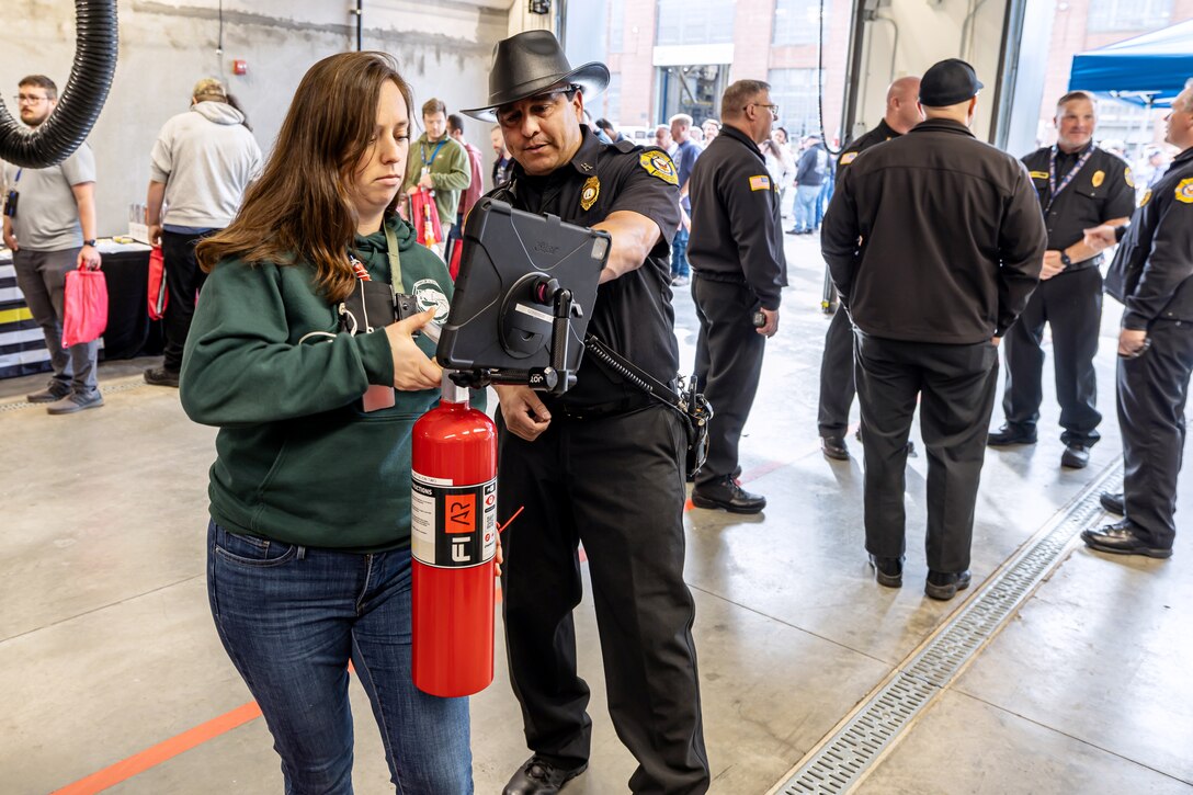 David Bustamante, fire inspector, Navy Region Northwest Fire and Emergency Services, shows Haley Redinger, radiological control technician, Code 105.3, Radiological Monitoring, how to operate an augmented reality fire extinguisher during a National Fire Prevention Week observance outside Building 435 at Puget Sound Naval Shipyard & Intermediate Maintenance Facility in Bremerton, Washington. (U.S. Navy photo by Jeb Fach)