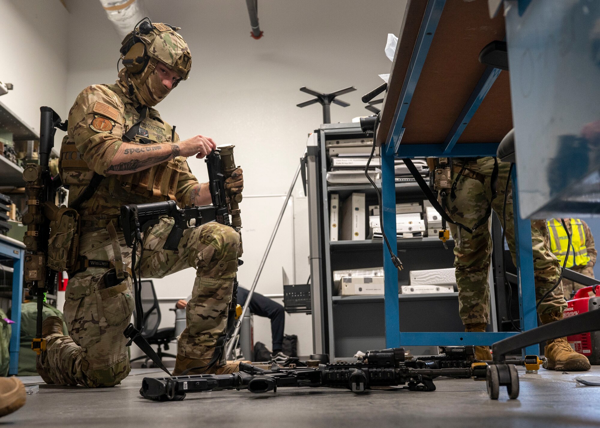 A man in military clothing kneels down and disassembles a rifle.