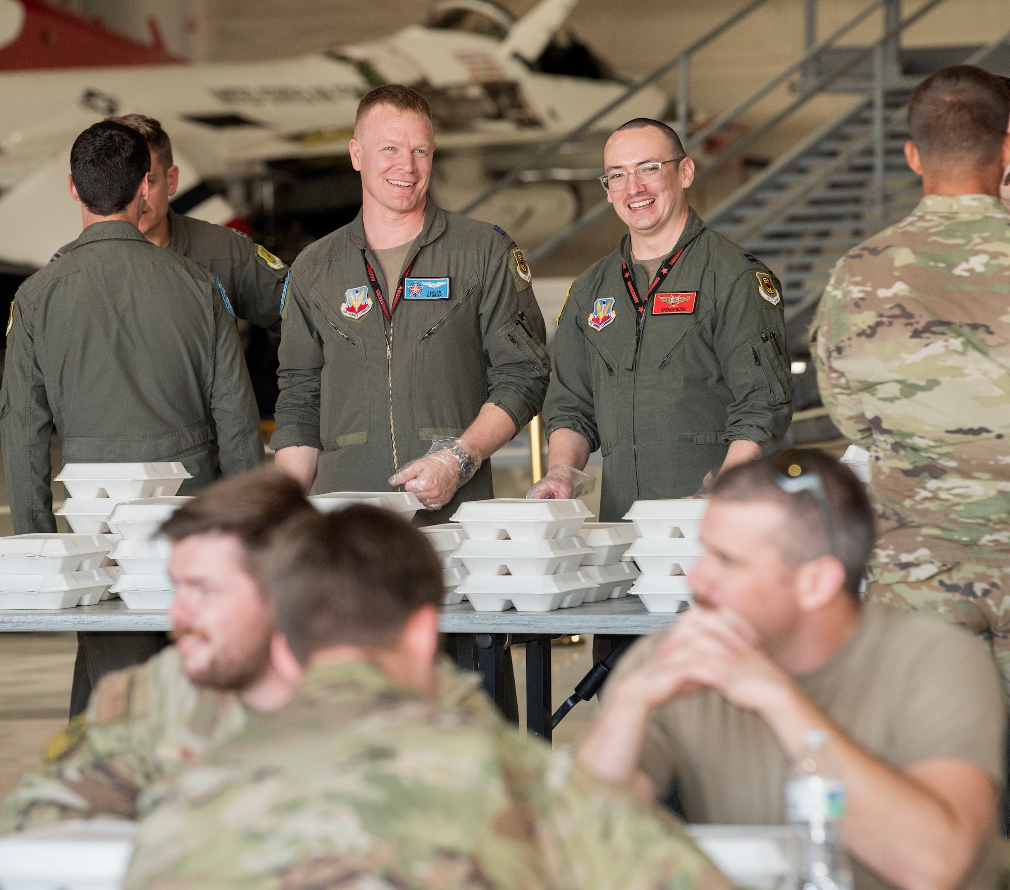 U.S. Air Force Capt. Tegan Cambier, an F-35A Lightning II pilot with the 65th Aggressors Squadron, left, and Capt. Spence Russi, an F-16 Fighting Falcon pilot with the 64th Aggressors Squadron, hand out barbecue to maintainers assigned to the 57th Wing at Nellis Air Force Base, Nevada, Oct. 28, 2024.