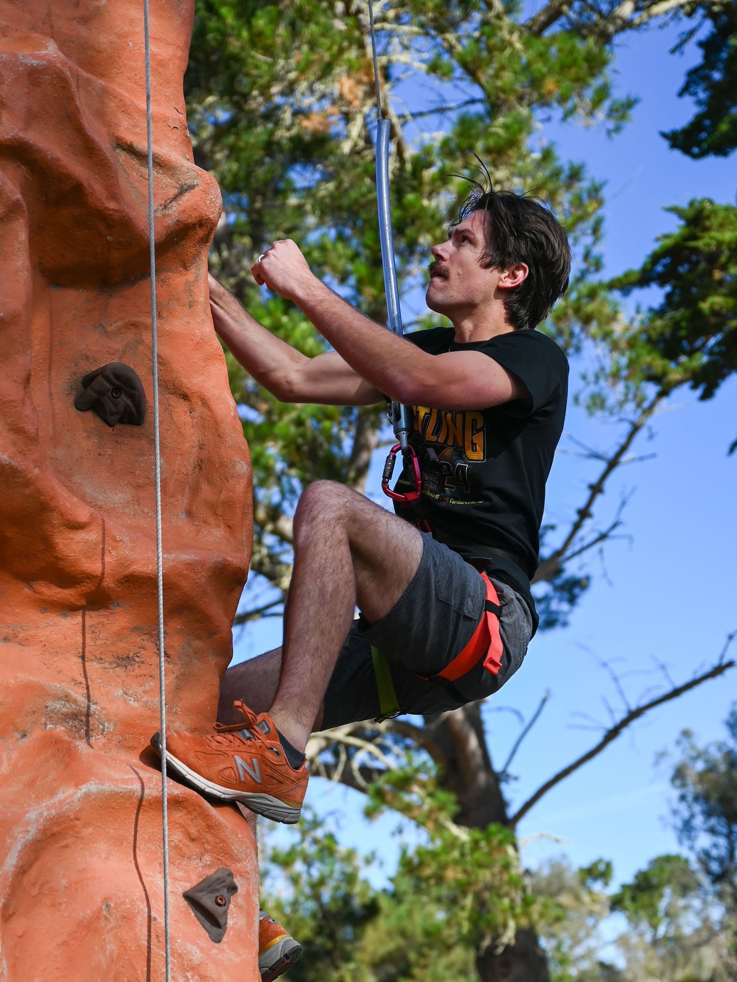 A man climbs a rock wall outside.